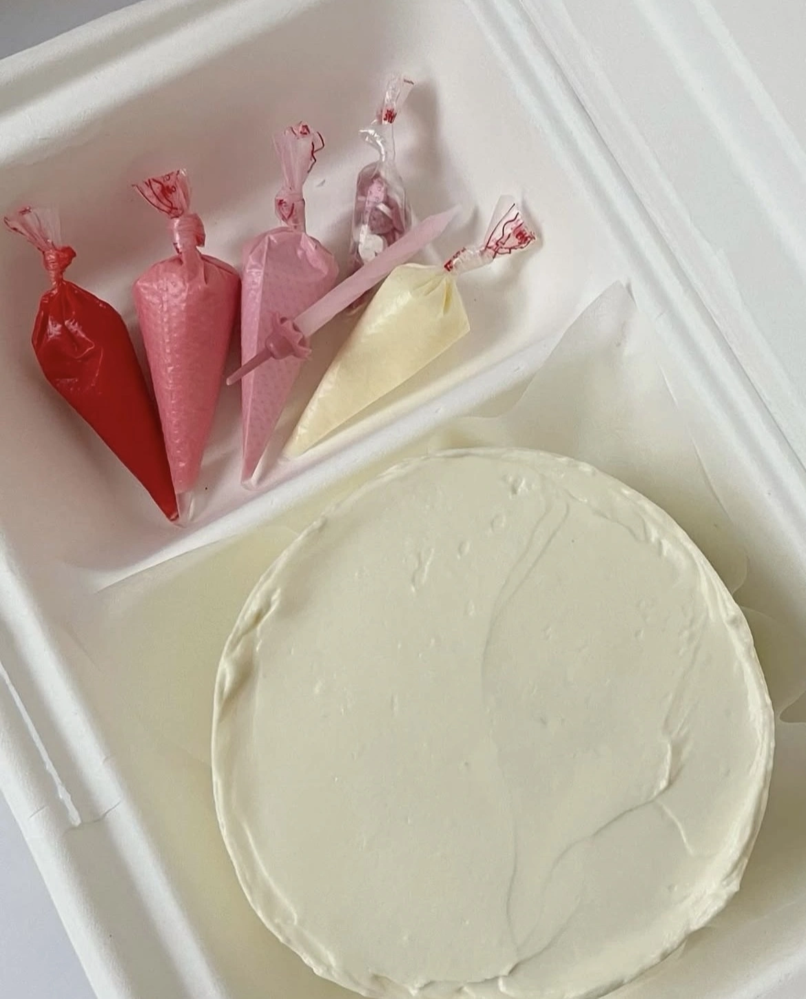 A regular sized bento cake with two decorating pipes and in a box