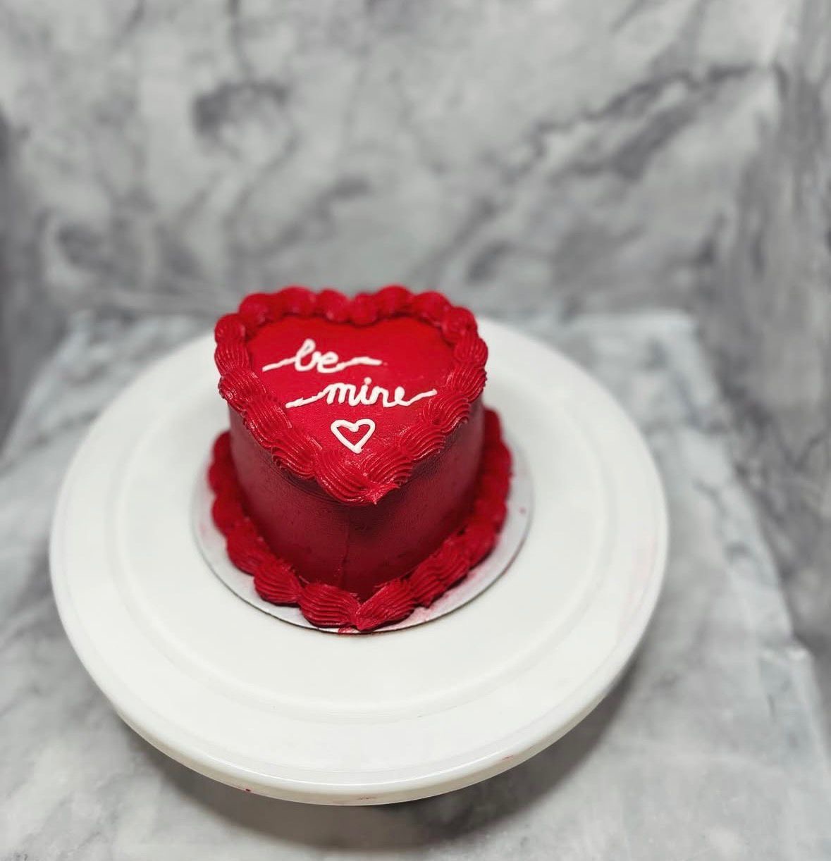 Red heart-shaped Valentine's Day bento cake with 'Be Mine' message and buttercream piping
